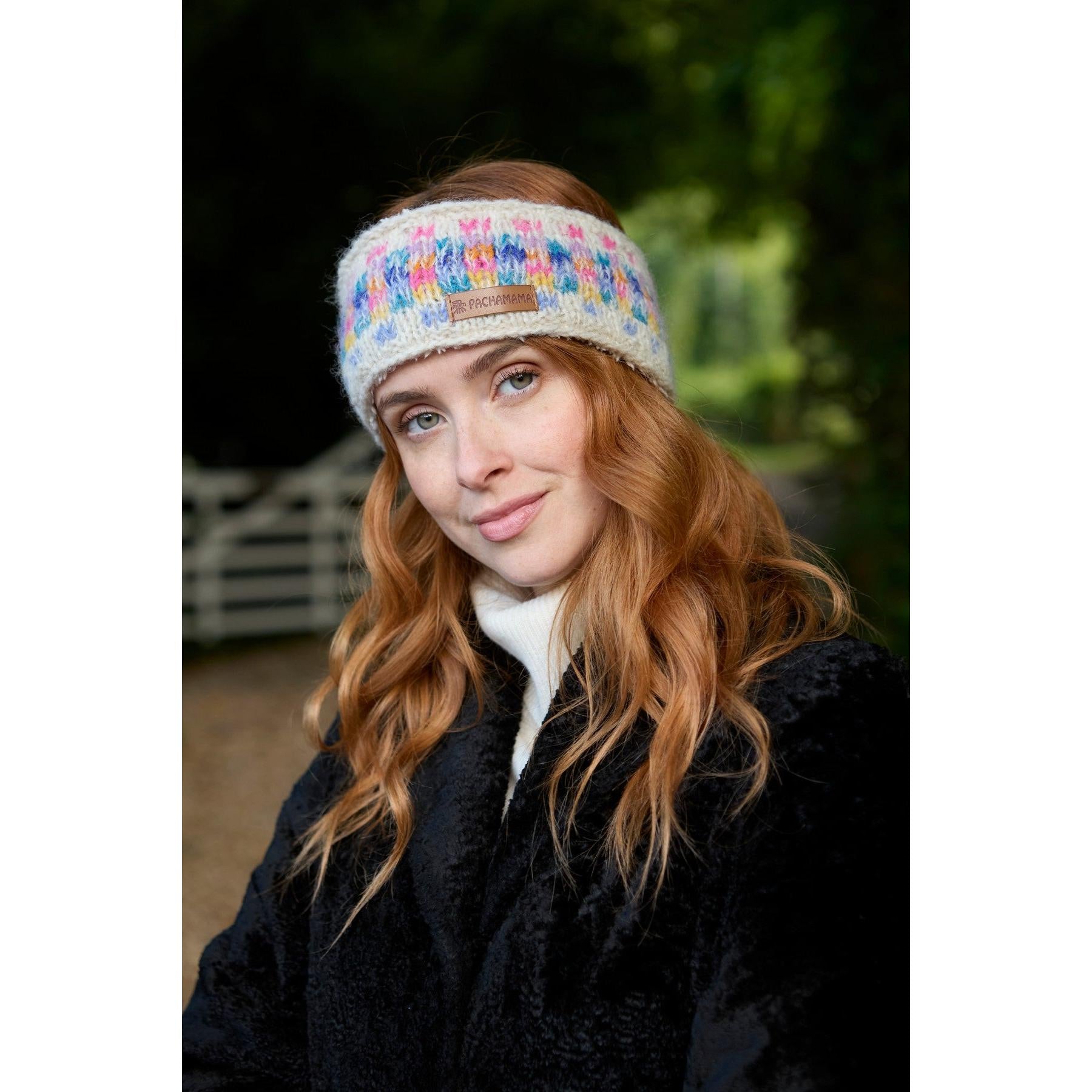 Woman wearing Pachamama Arundel Headband in oatmeal with colorful knit pattern, outdoors.