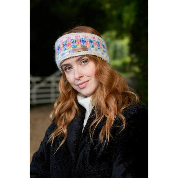 Woman wearing Pachamama Arundel Headband in oatmeal with colorful knit pattern, outdoors.