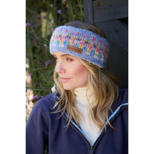 Pachamama Arundel Sky headband with multicolor knit pattern, worn by woman outdoors, breathable and stylish for winter wear.