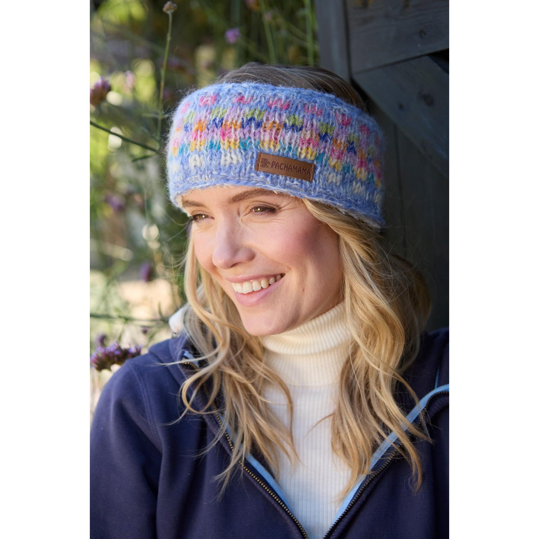 Woman wearing a colorful Pachamama Arundel Sky headband outdoors, smiling, with floral background.