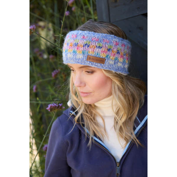 Pachamama Arundel Sky headband, multicolor knit, soft warm fabric, worn by woman outdoors with flowers, stylish winter accessory.