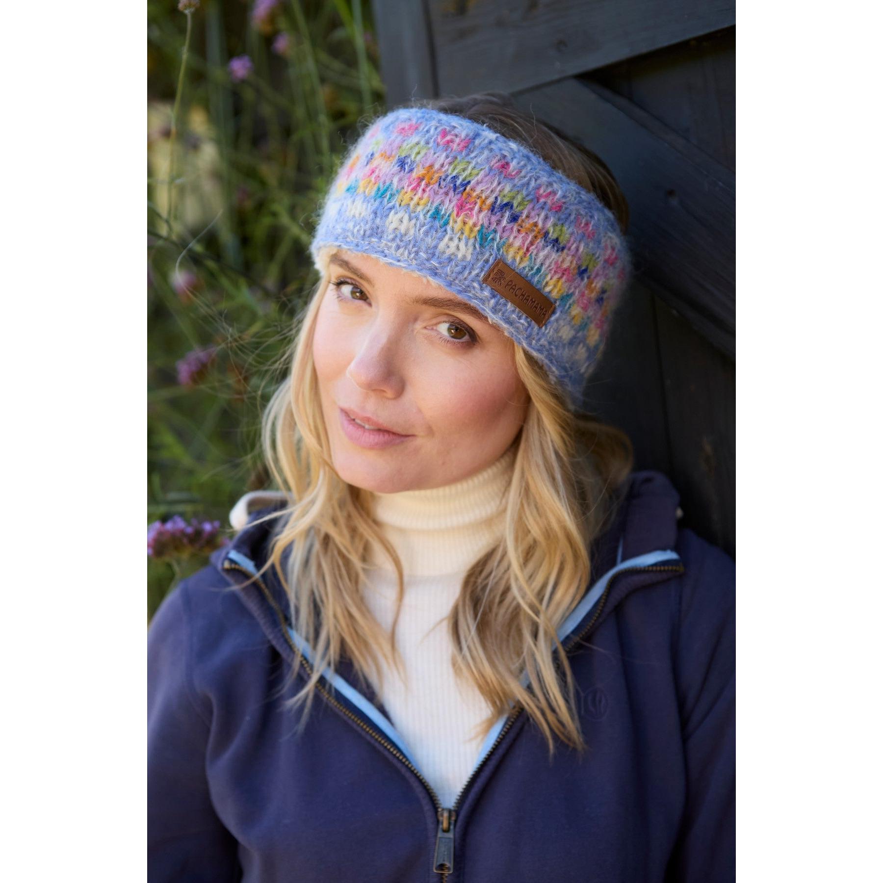 Pachamama Arundel Sky headband with colorful knitted pattern, worn by a woman outdoors, featuring a leather logo patch.