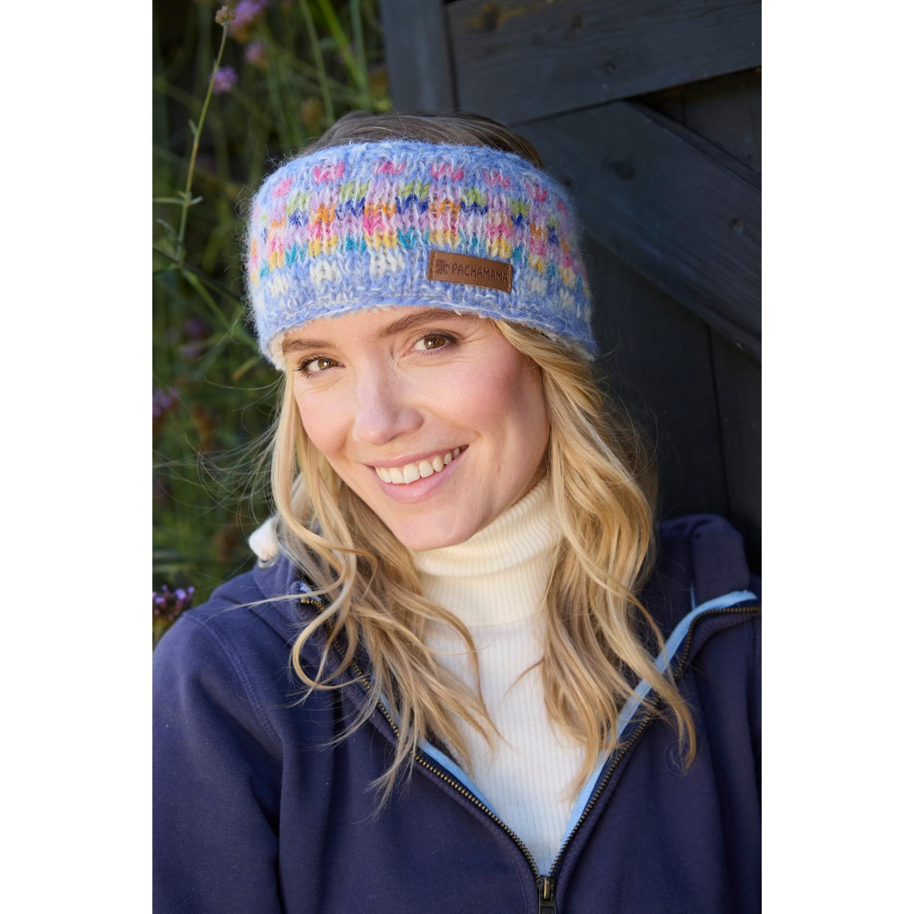 Pachamama Arundel Sky headband, colorful knitted winter accessory on smiling woman outdoors, cozy and stylish design.