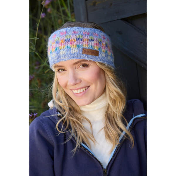 Pachamama Arundel Sky headband, colorful knitted winter accessory on smiling woman outdoors, cozy and stylish design.