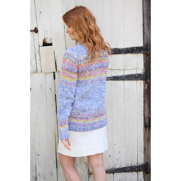 Pachamama Arundel Sweater Sky featuring colorful, patterned knit design on a woman standing outdoors by a rustic wooden door.