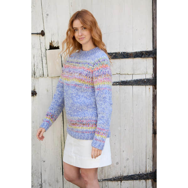 Pachamama Arundel Sweater Sky in pastel-colored knit, worn by a woman outdoors against rustic wooden background.