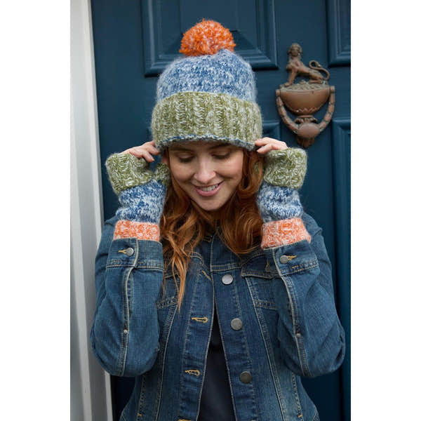 Woman wearing a multicolored knit bobble beanie and fingerless gloves, standing in front of a blue door.