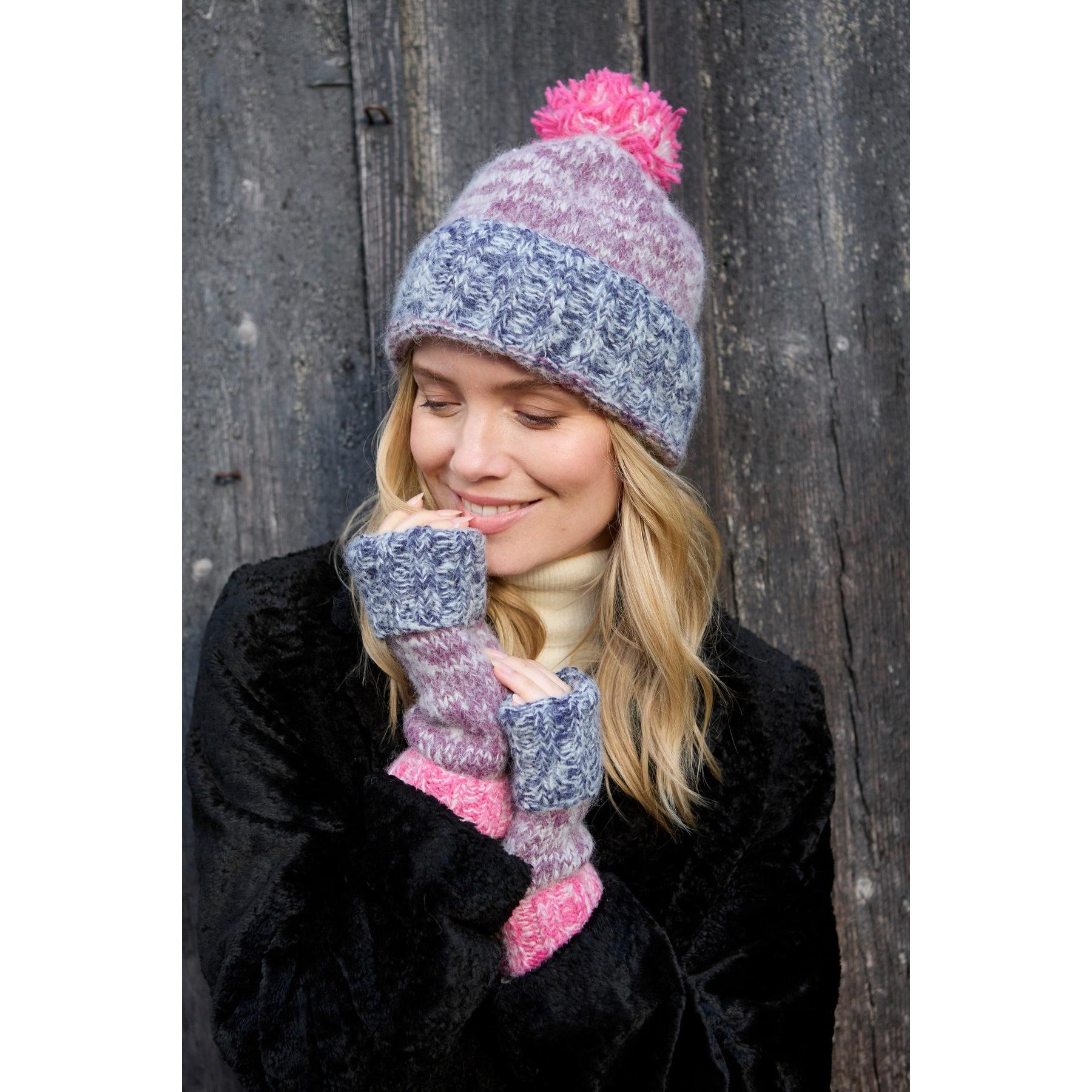Pachamama Berlin purple bobble beanie and matching knit mittens worn by woman, cozy winter accessories, black coat, outdoor setting.