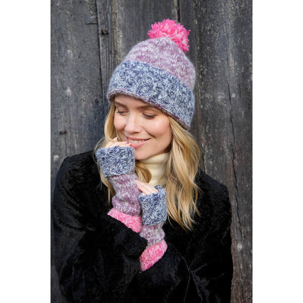 Pachamama Berlin purple bobble beanie and matching knit mittens worn by woman, cozy winter accessories, black coat, outdoor setting.
