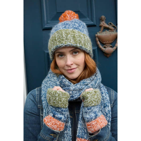 Pachamama Berlin blue and green knit handwarmer, beanie, and scarf set with orange accents, worn by a smiling woman outdoors.