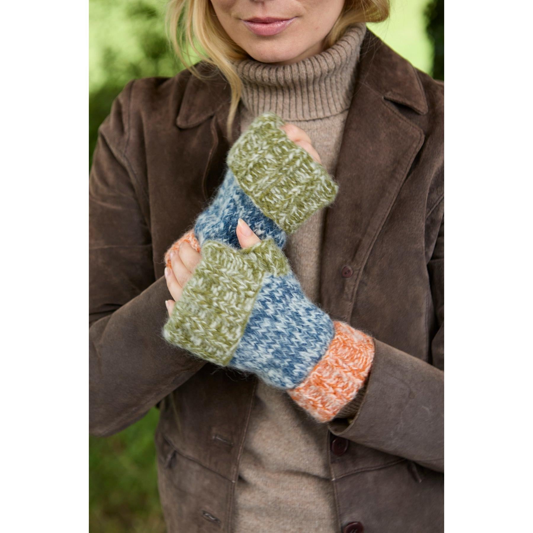Pachamama Berlin blue and green handwarmer gloves worn by a woman in a brown jacket outdoors.
