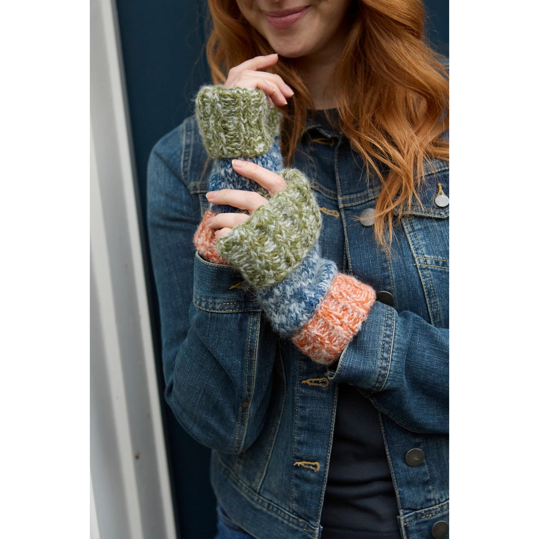 Handwarmer gloves in blue, green, orange, and patterned knit, held by a woman in a denim jacket.