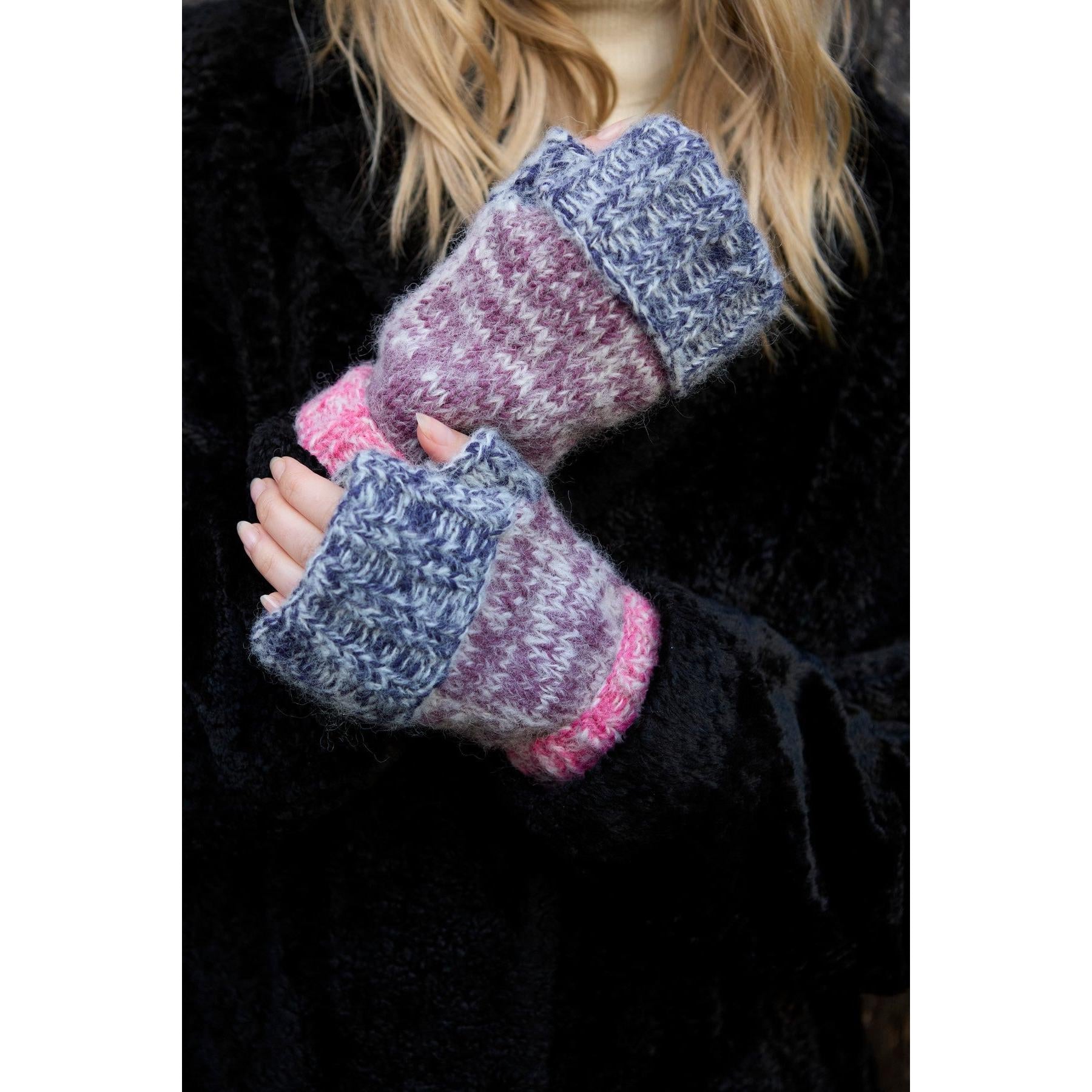 Pachamama Berlin purple handwarmer gloves with grey, pink, and blue knit patterns, worn by a person in a black coat.
