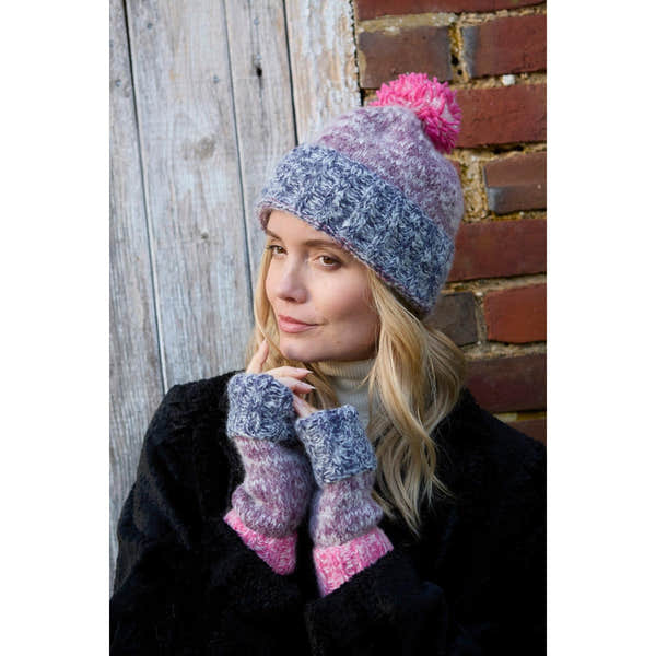 Pachamama Berlin purple knit hat and fingerless gloves, soft winter accessories, model outdoors near brick wall and wooden background.