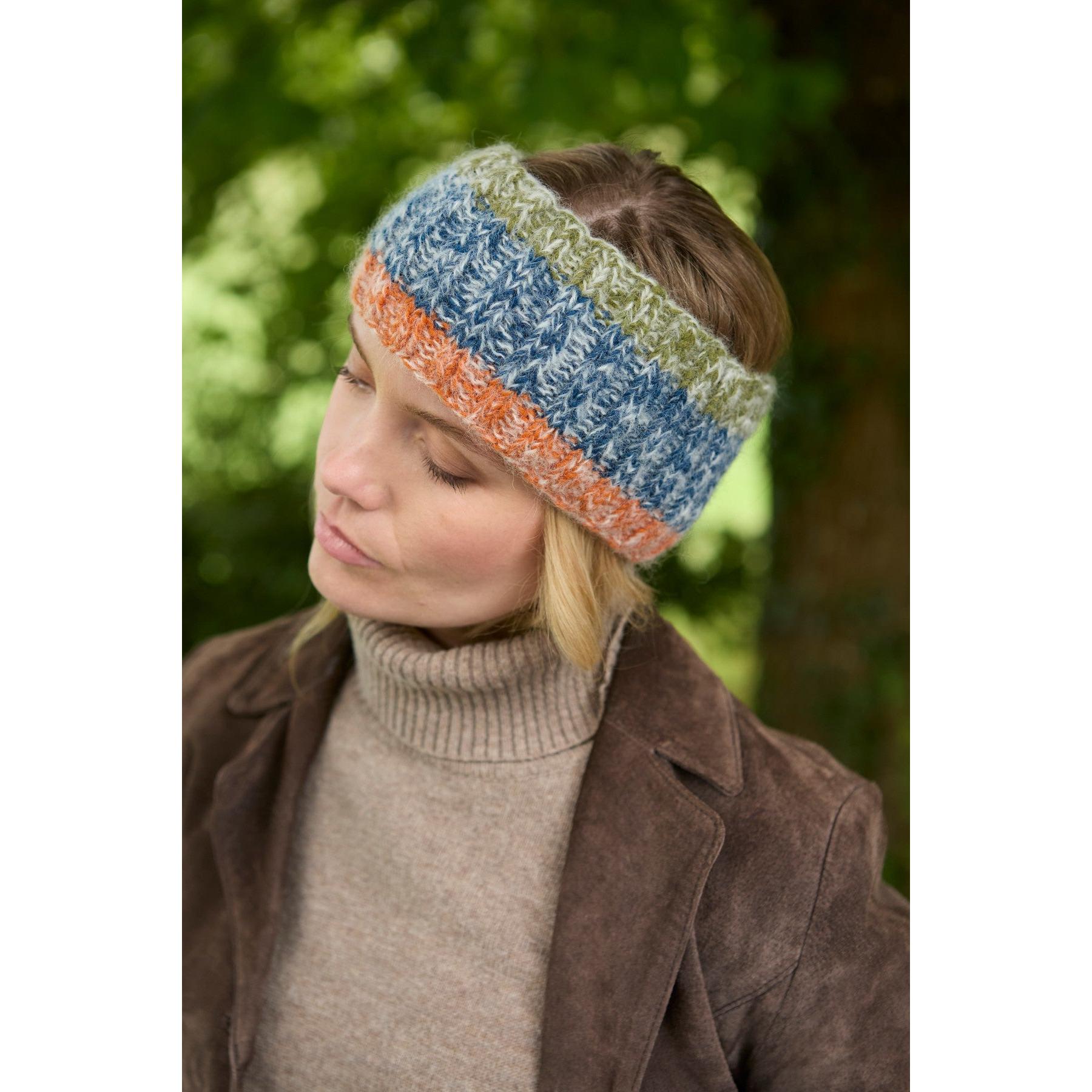 Pachamama Berlin blue and multicolor knit headband, cozy and stylish, worn by woman outdoors with green foliage background.