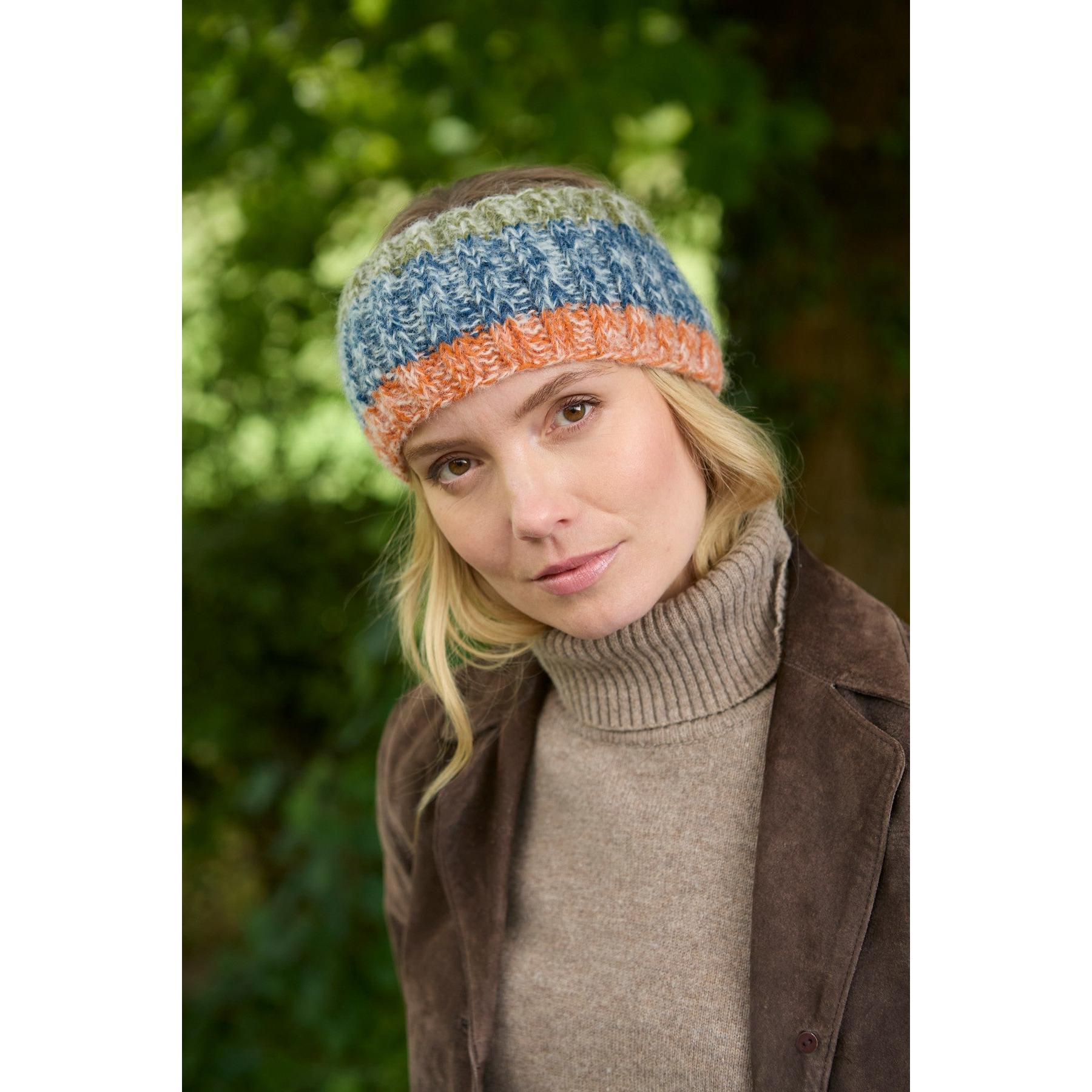 Woman wearing a blue, orange, and green knitted Pachamama Berlin headband outdoors in nature.