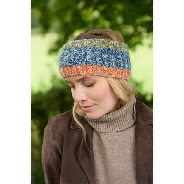 Pachamama Berlin blue multicolor knit headband, cozy winter accessory for women, outdoors, against green blurred background.