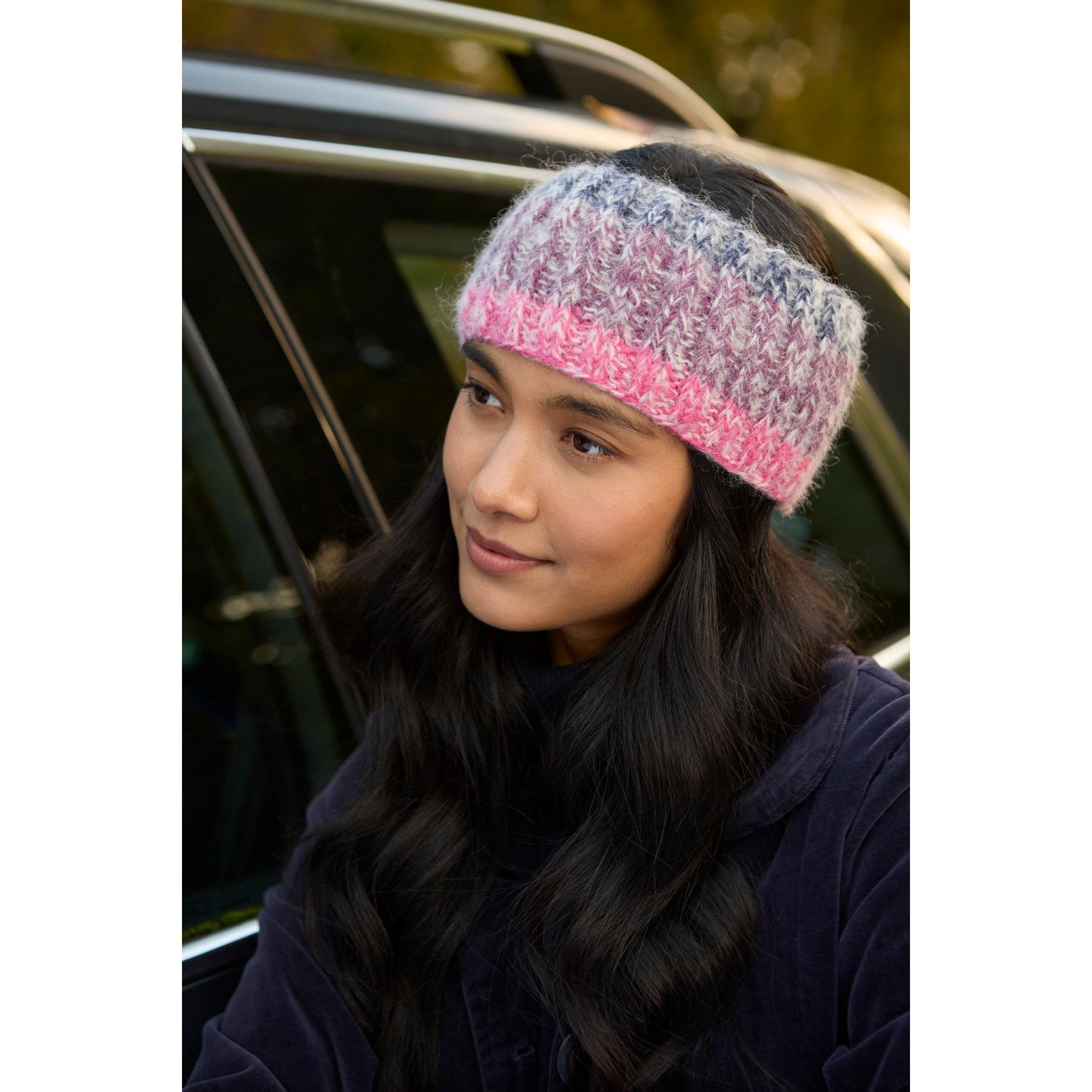 Pachamama Berlin purple headband, knitted with pink, gray, and purple tones, worn by a woman outdoors.