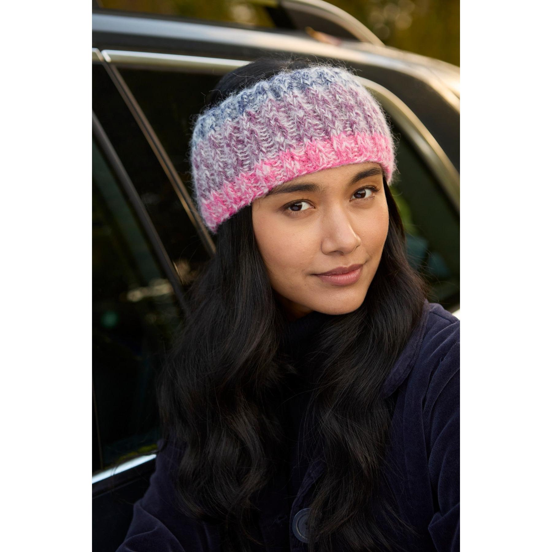 Woman wearing purple Pachamama Berlin knit headband with pink and gray pattern close-up photo.
