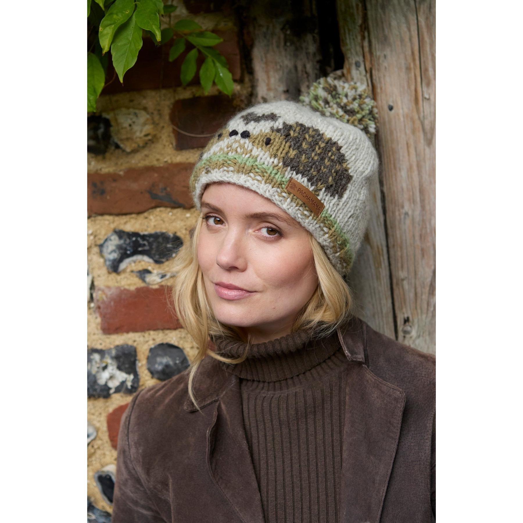 Pachamama Hedgehog bobble beanie with animal design, knitted texture, and colorful details, worn by a woman in outdoor setting.