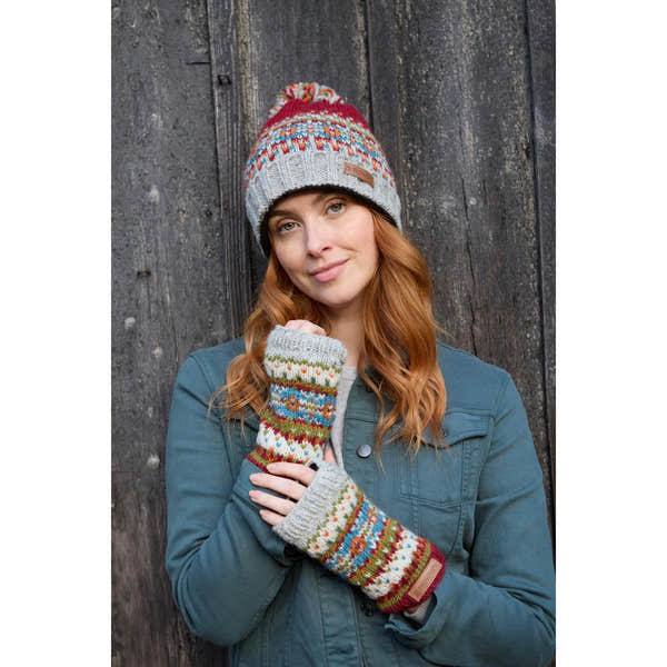 Pachamama Iona Burgundy wool handwarmer gloves and knit beanie hat worn by woman against wooden background.