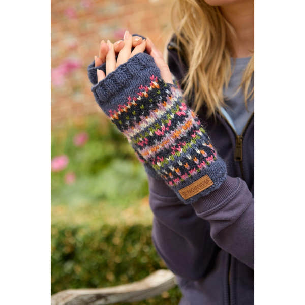 Pachamama Iona Handwarmer Denim, colorful knitted fingerless glove with floral pattern, leather logo patch, worn by woman outdoors.