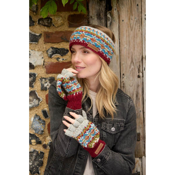 Pachamama Iona Headband Burgundy with multicolor knit pattern, paired with matching fingerless gloves, worn by a woman outdoors.