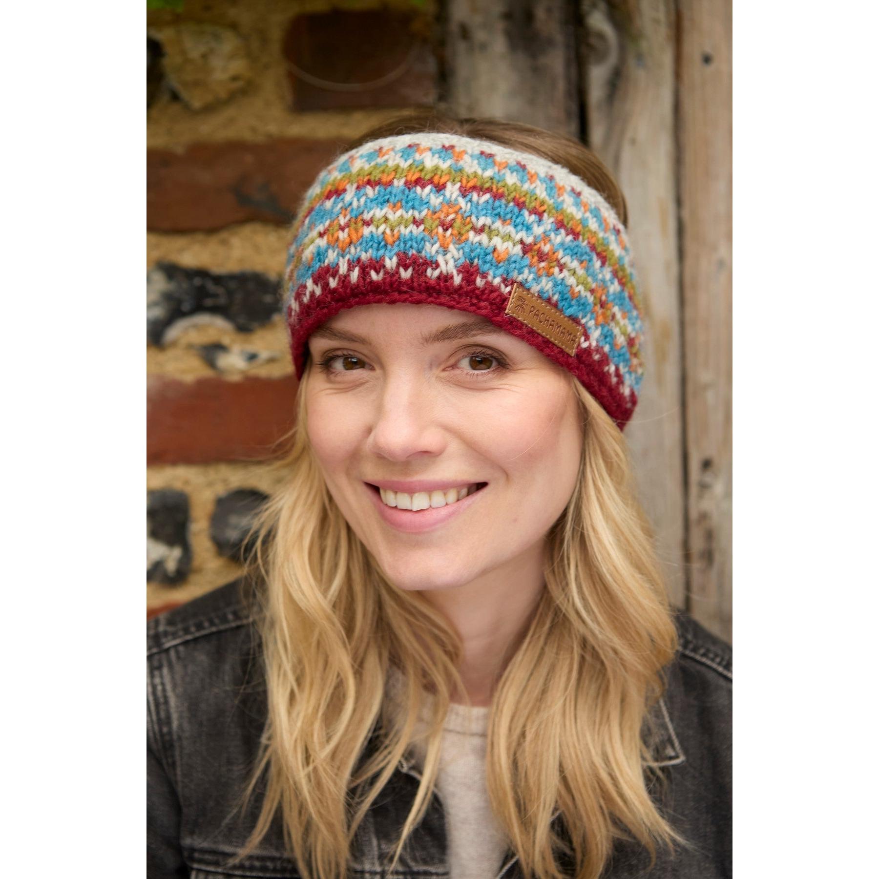 Woman wearing a burgundy Pachamama Iona knit headband with colorful pattern, outdoor background.
