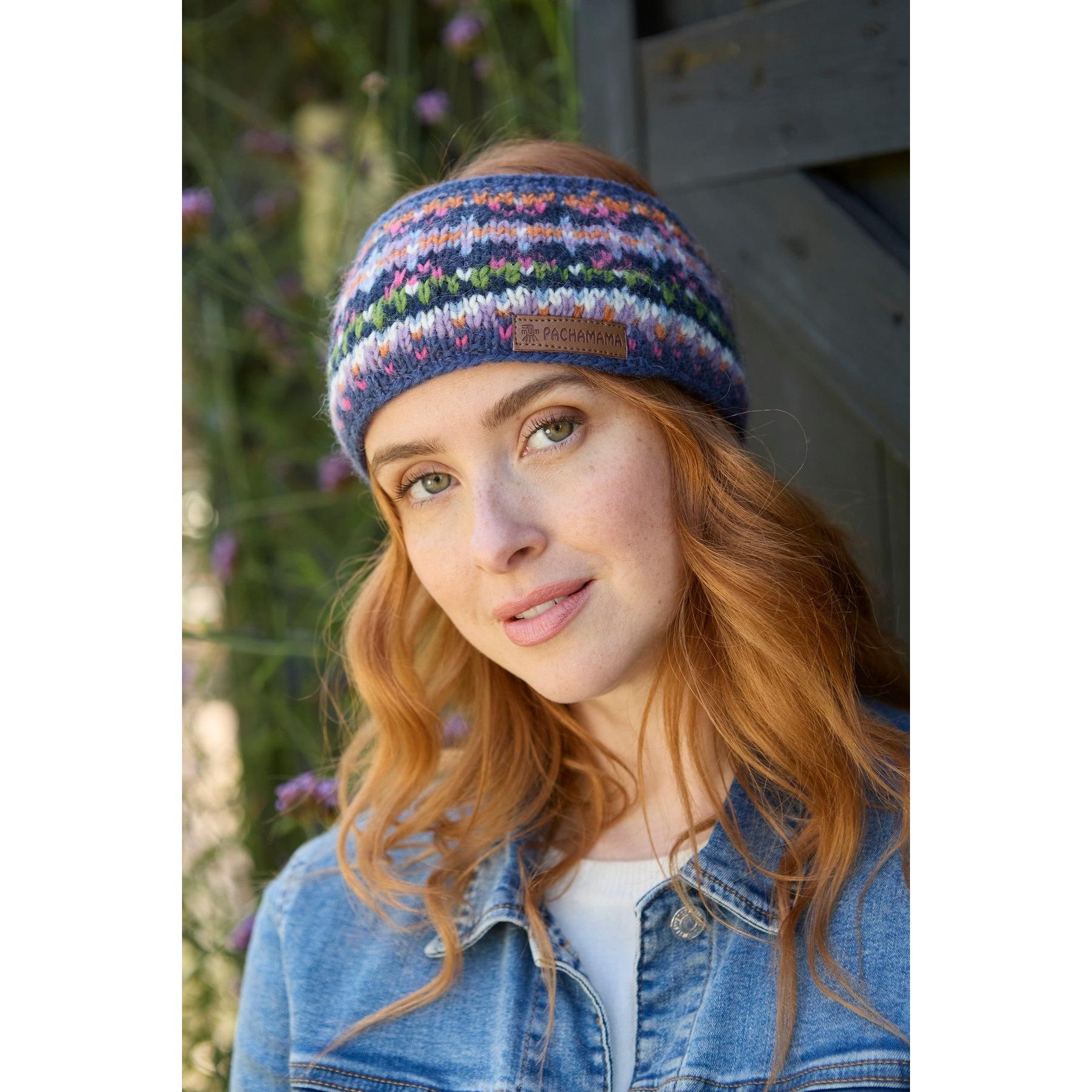 Woman wearing a Pachamama Iona denim headband with colorful knit pattern, outdoors with greenery.