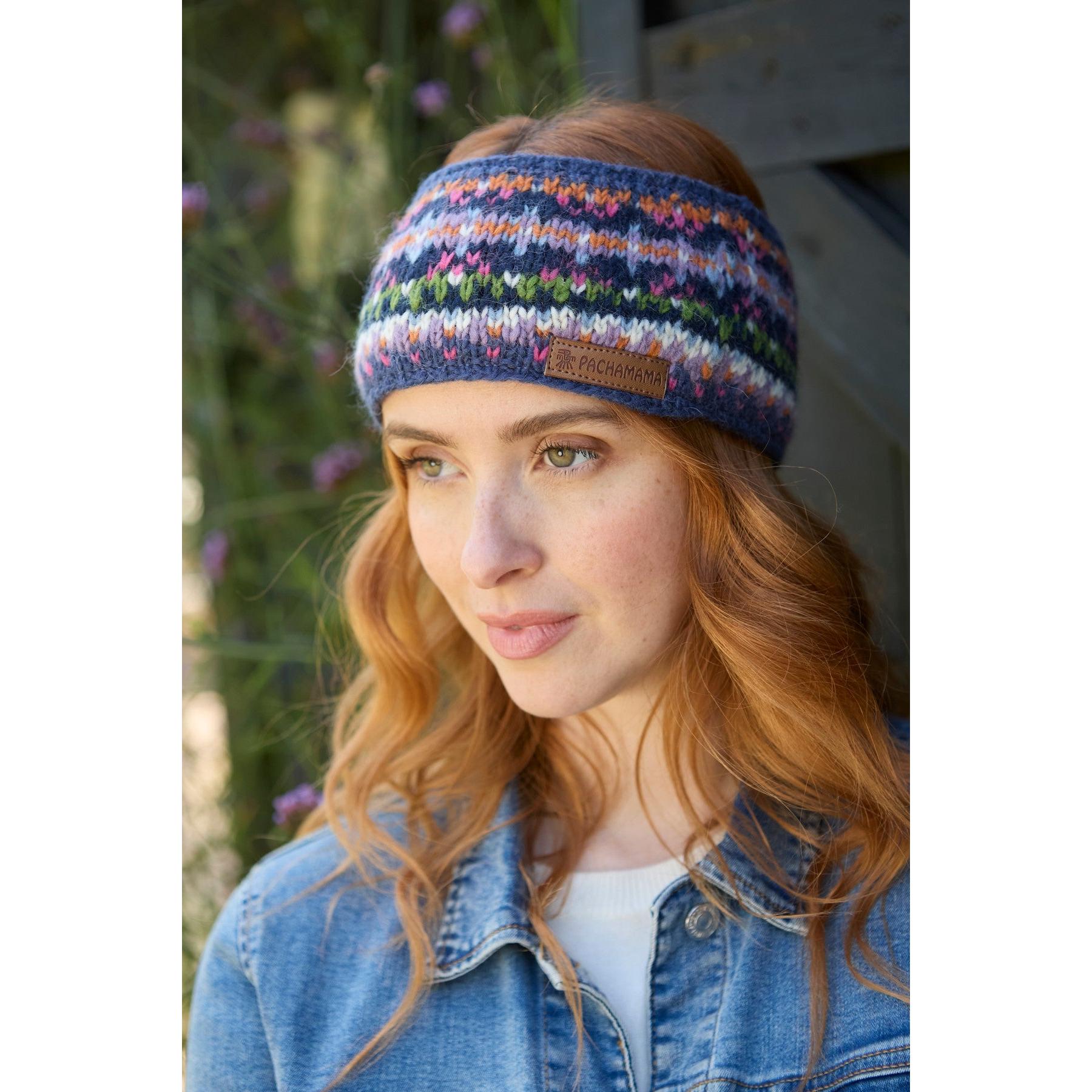 Pachamama Iona headband in denim with colorful knit pattern and leather logo patch, worn by a woman outdoors.
