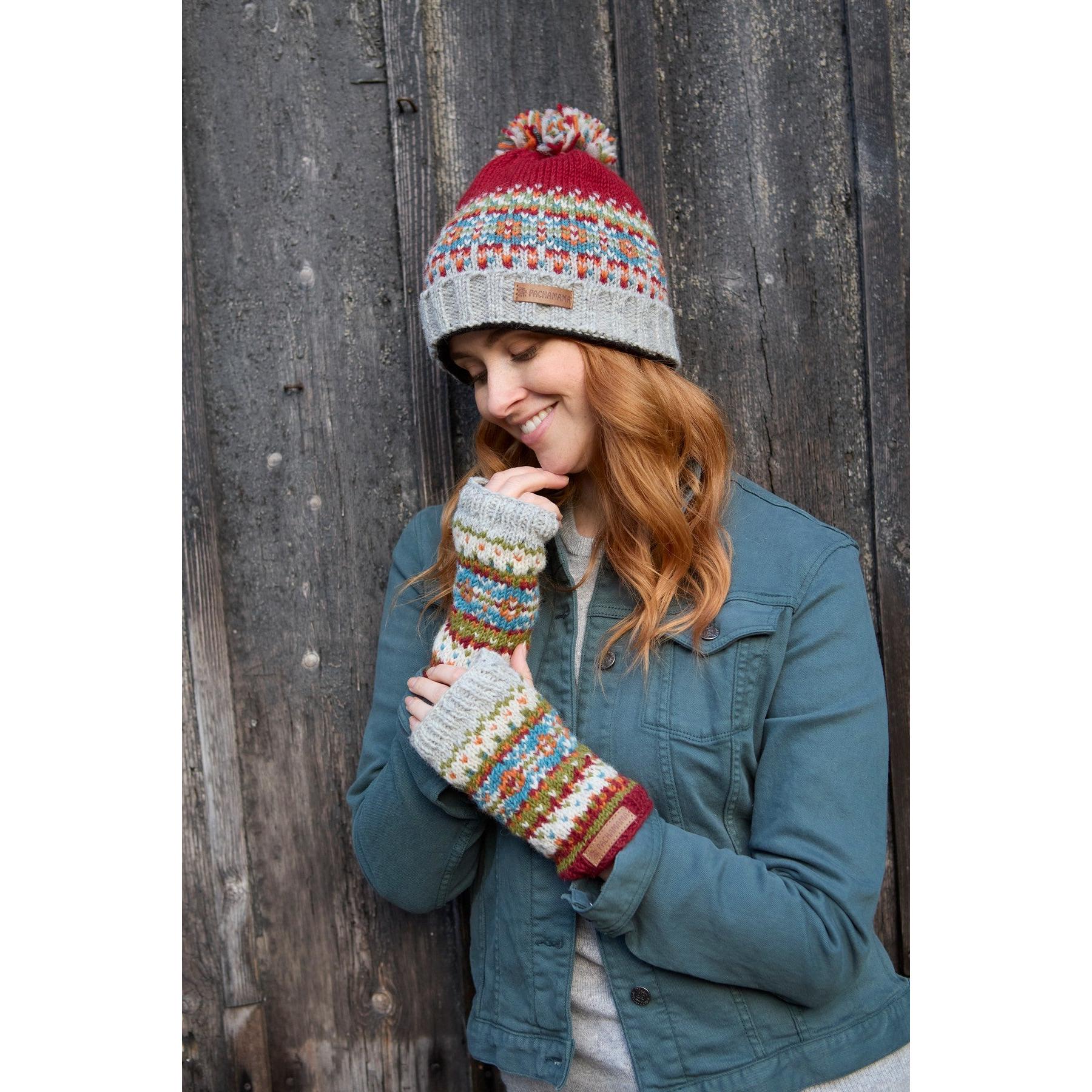 Pachamama Iona Roll Back Bobble Beanie Burgundy with colorful knit pattern and pom-pom, worn by a woman with matching fingerless gloves.