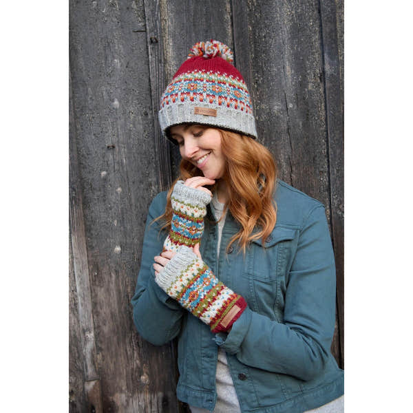 Pachamama Iona Roll Back Bobble Beanie Burgundy with colorful knit pattern and pom-pom, worn by a woman with matching fingerless gloves.