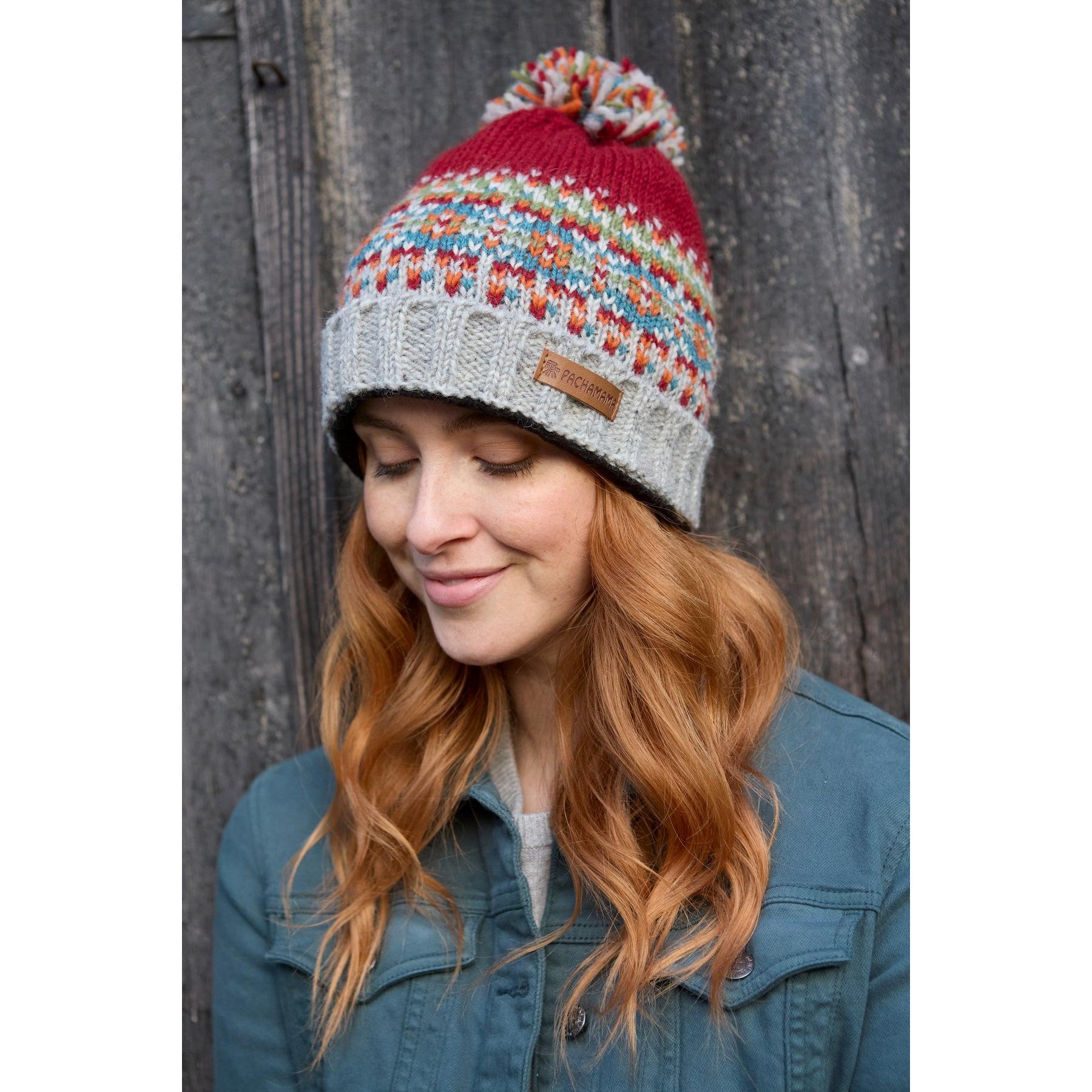 Women wearing burgundy Pachamama Iona Roll Back Bobble Beanie with colorful pattern and pom-pom, outdoor winter accessory.