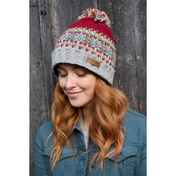 Women wearing burgundy Pachamama Iona Roll Back Bobble Beanie with colorful pattern and pom-pom, outdoor winter accessory.