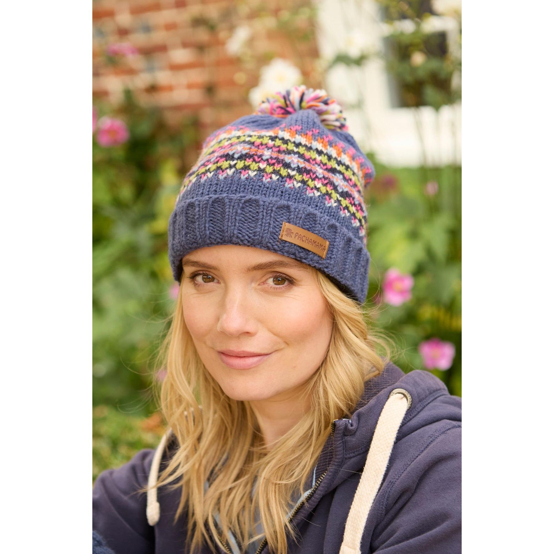 Pachamama Iona Roll Back Bobble Beanie in denim with colorful knit pattern and pom pom, worn by woman outdoors.