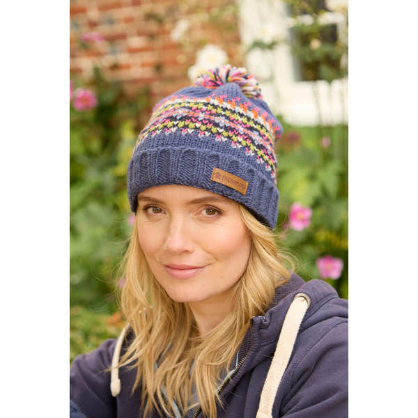Pachamama Iona Roll Back Bobble Beanie in denim with colorful knit pattern and pom pom, worn by woman outdoors.