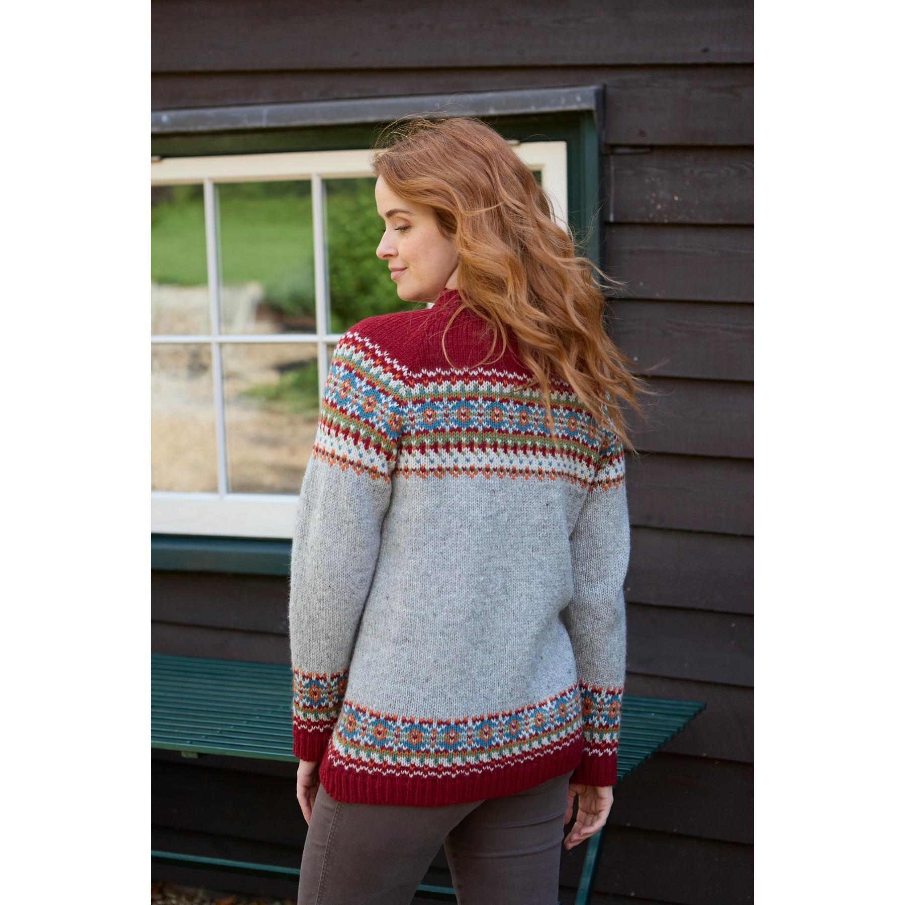 Women wearing Burgundy Pachamama Iona Sweater with colorful Fair Isle pattern, standing outdoors near a dark wooden building.