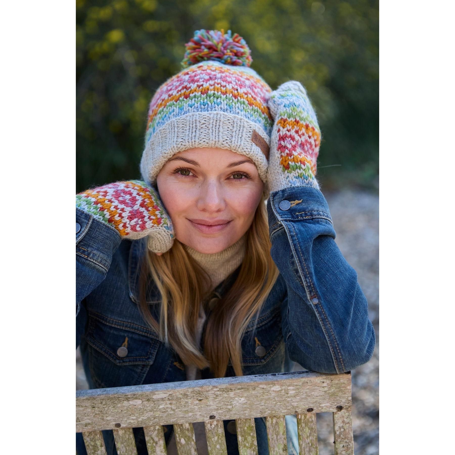 Pachamama Killarney Bobble Beanie in oatmeal, colorful merino wool, worn by woman outdoors, cozy winter hat with pom-pom.
