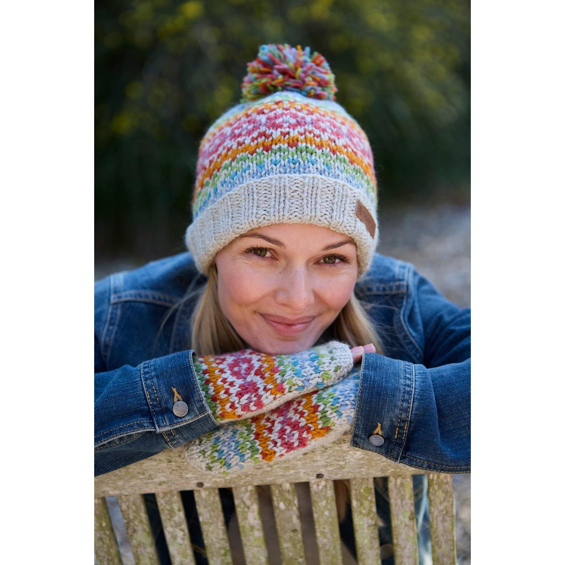Woman wearing Pachamama Killarney Bobble Beanie and matching merino mittens in oatmeal, outdoor setting.