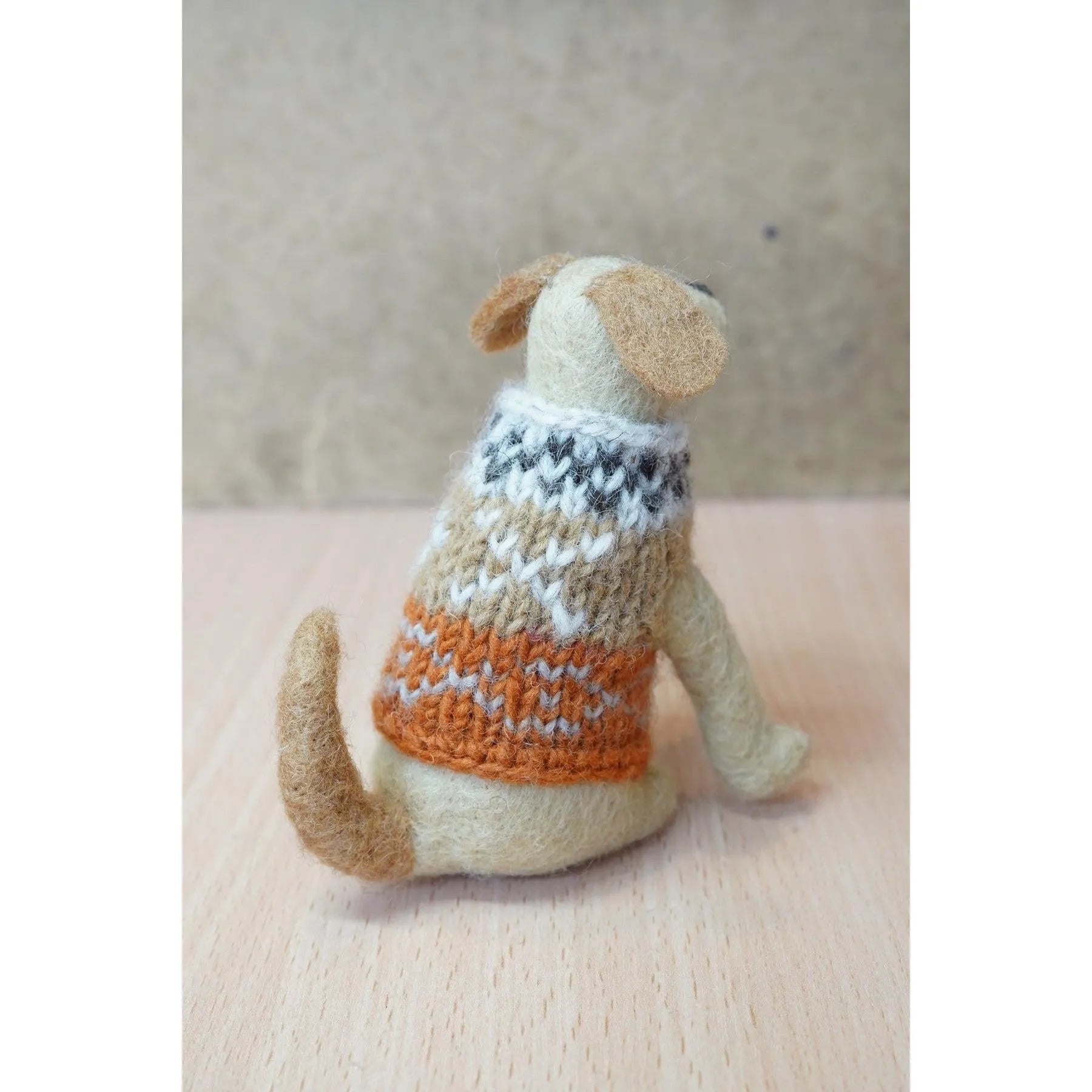 Felted Labrador dog wearing a multicolored knitted sweater, sitting on a wooden surface.