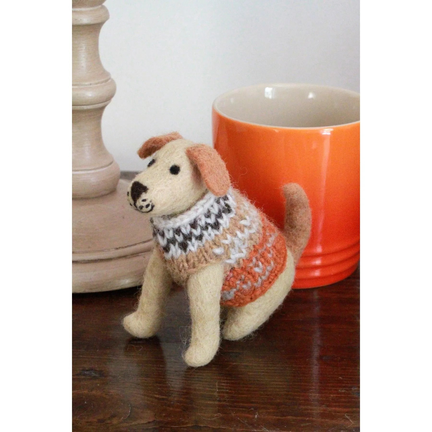 Felted Labrador dog plush toy with a knitted sweater, placed next to an orange mug and beige decorative item.