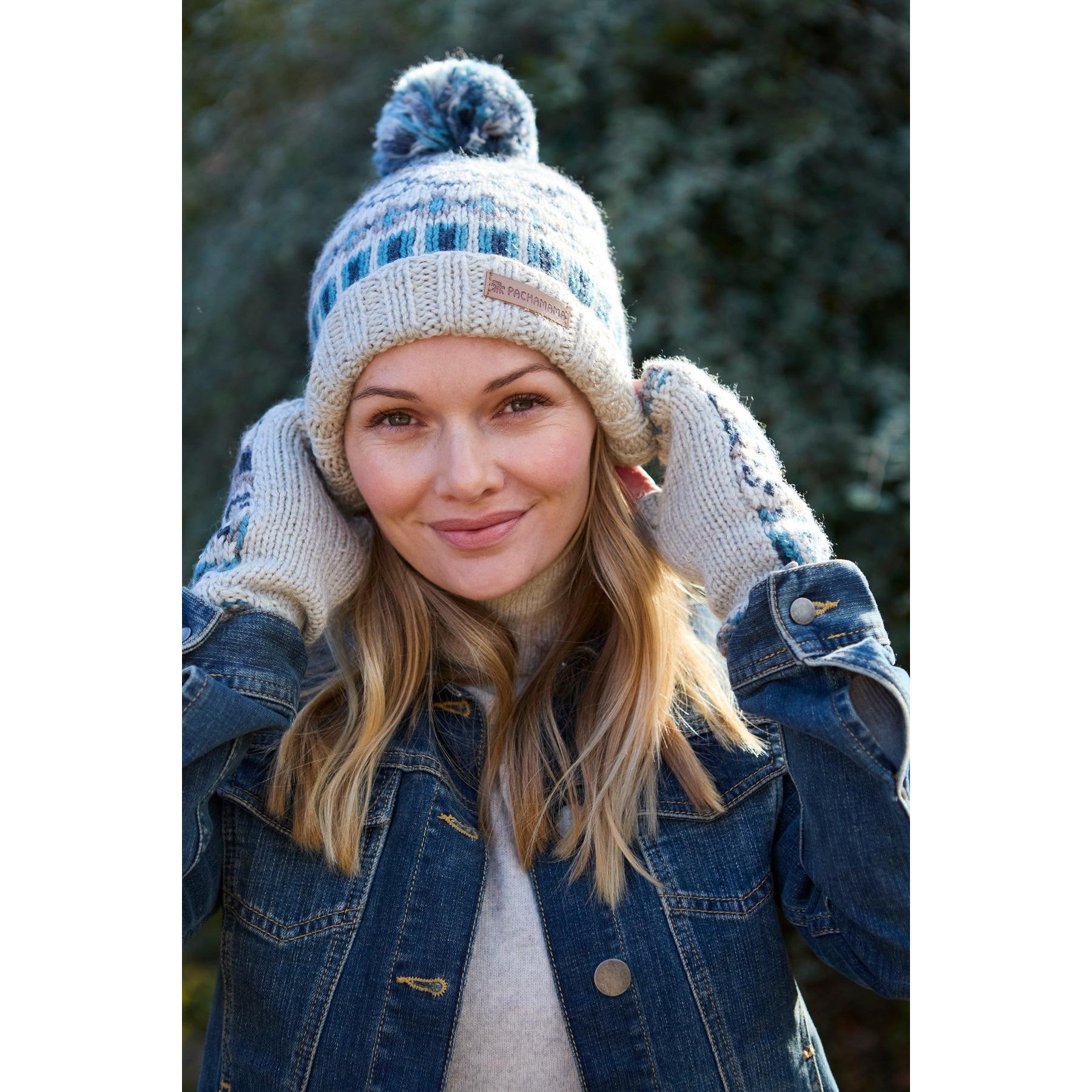 Woman wearing blue and cream Pachamama Loch Fyne pure merino handwarmer hat with pom-pom, outdoor winter fashion.