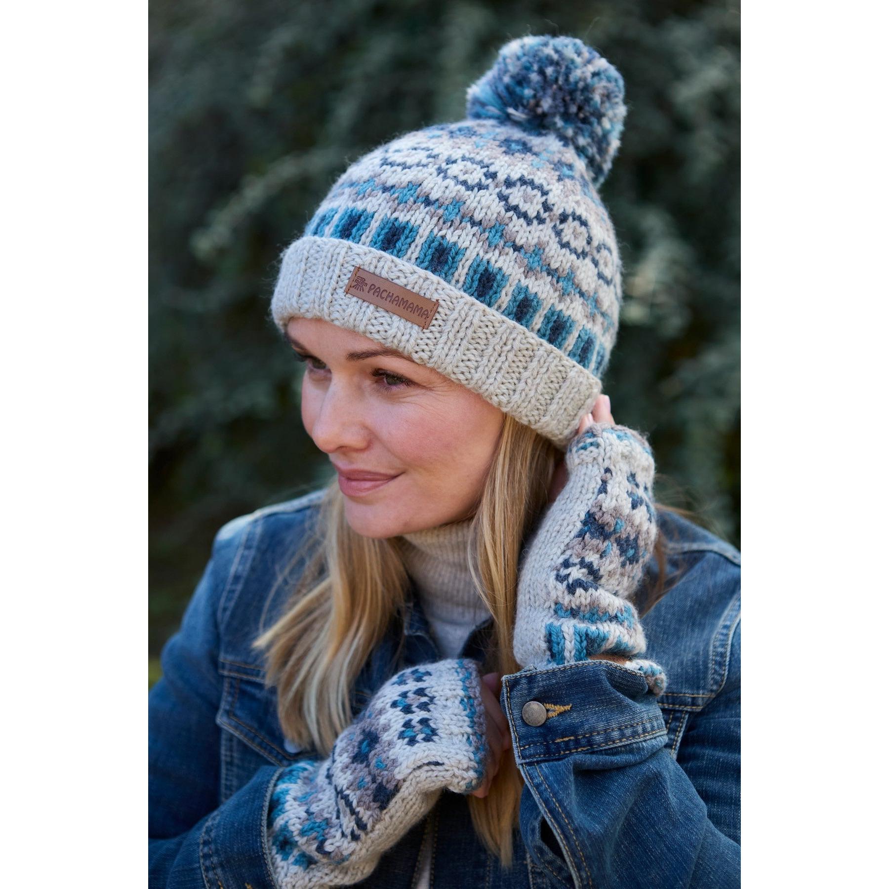 Blue Merino wool knit beanie with pom-pom, rolled brim, and Pachamama logo tag, worn with matching patterned gloves.