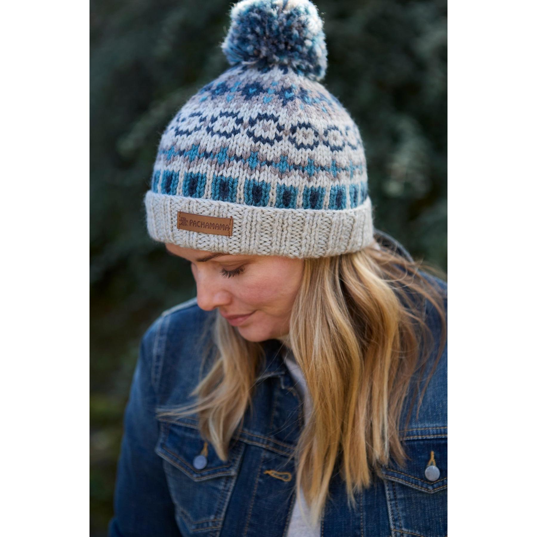 Blue merino wool bobble beanie with Fair Isle pattern and rolled brim, featuring a Pachamama leather logo patch.