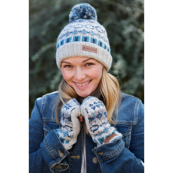 Woman wearing blue and beige Merino knit roll-up beanie hat and matching mittens, outdoors, smiling.