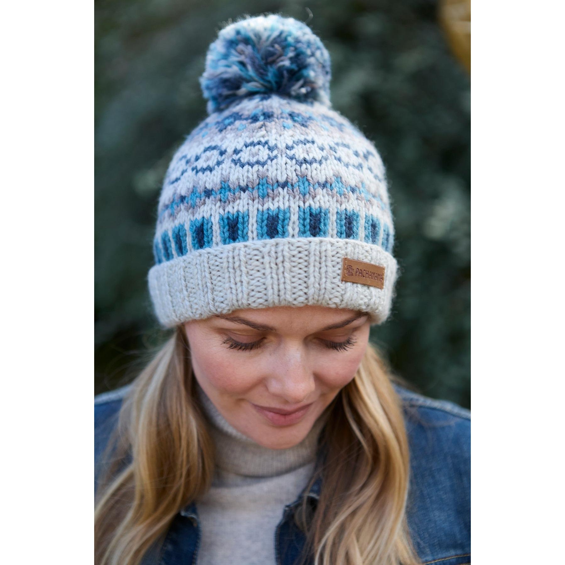 Pachamama Loch Fyne Roll Back Bobble Beanie in pure merino wool, blue and white Nordic pattern, with pom-pom, worn by woman with blonde hair.