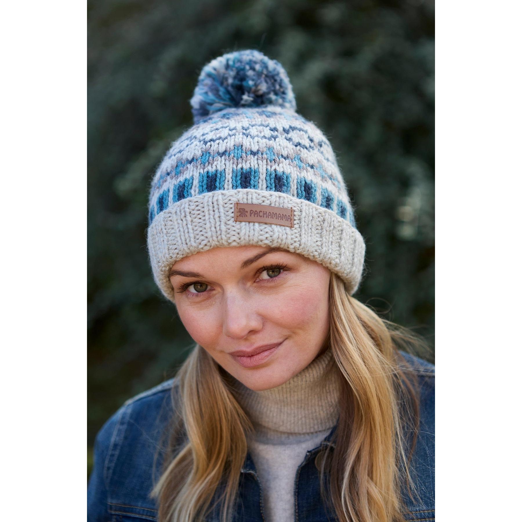 Blue and beige Merino wool roll-back bobble beanie with a pom-pom, featuring a Pachamama label, worn by a woman outdoors.