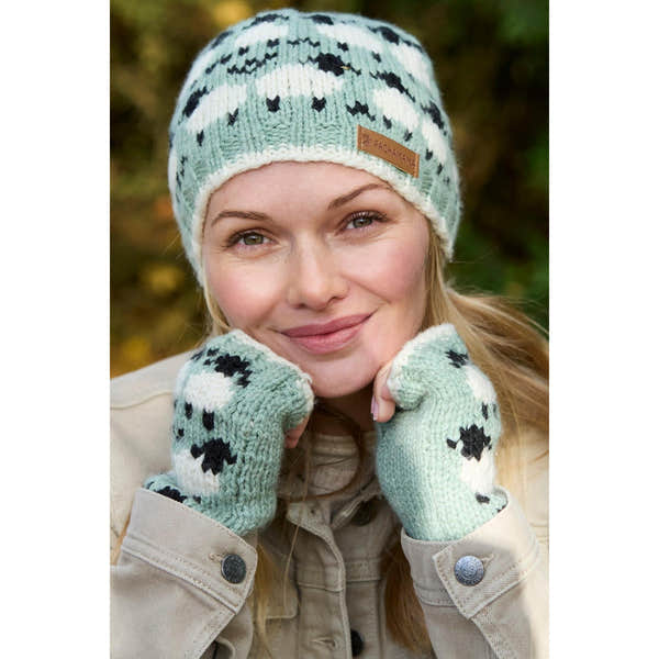 Pachamama Merino sheep handwarmer and beanie set in green with black and white spotted pattern, soft wool texture, outdoors.