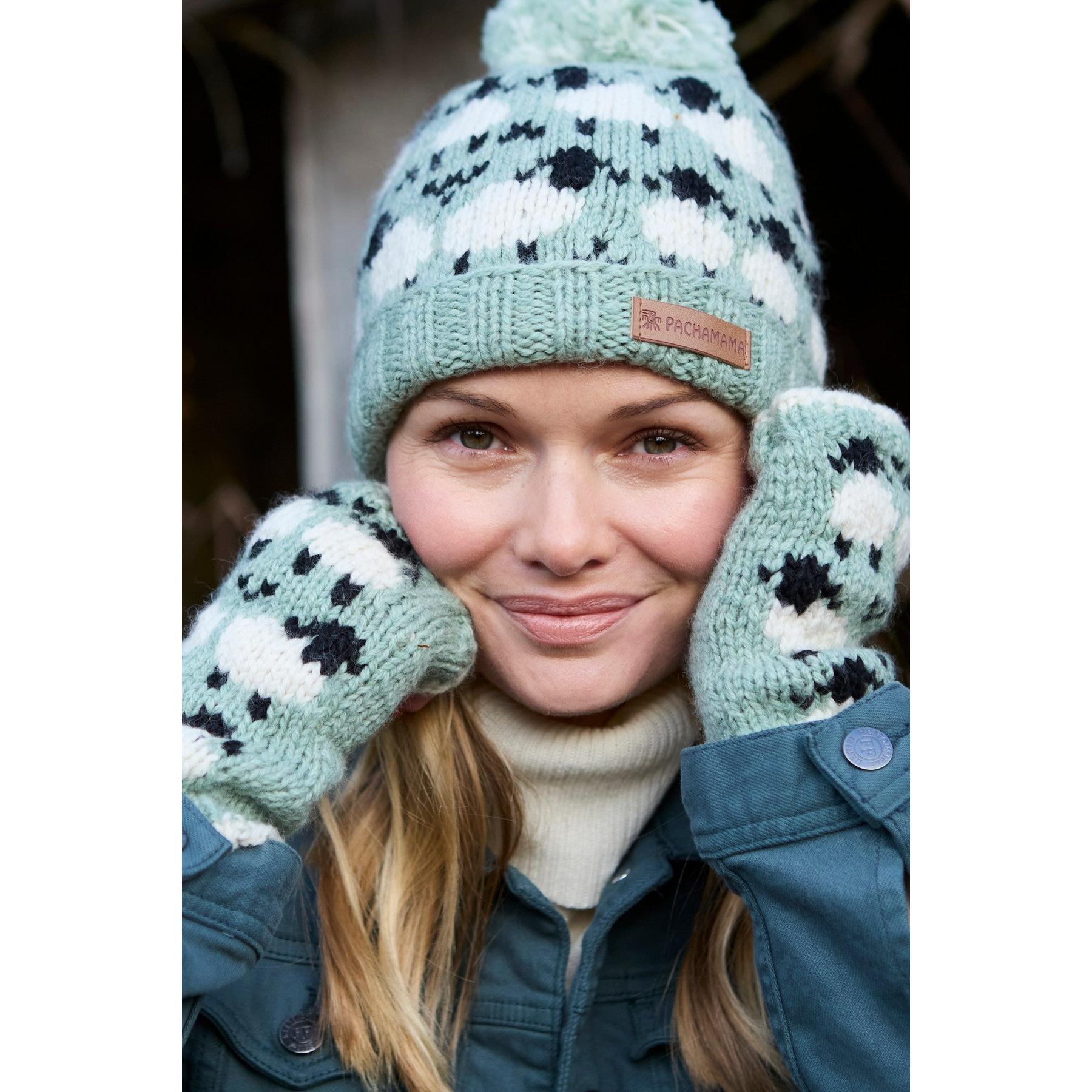 Woman wearing green Pachamama Merino sheep roll-back bobble beanie and matching mittens, smiling outdoors.