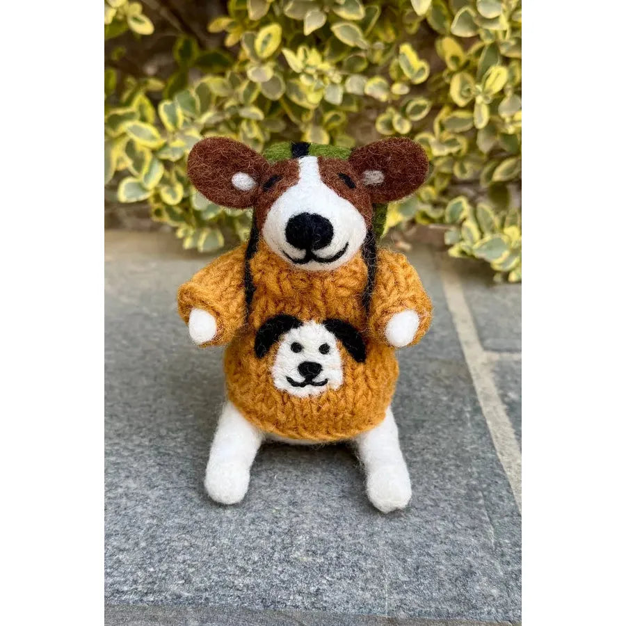 Felted Pachamama Rambling Roger plush toy with dog character in an orange sweater, standing outdoors with green foliage backdrop.